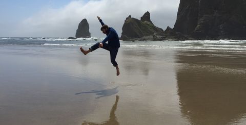 James jumping in front of large rocks in the ocean.