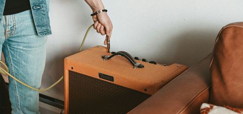 Someone out-of-frame plugging a cable into an orange guitar amp